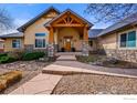 Inviting entrance boasting stone accents, a covered porch with wood beams, and a beautifully landscaped front yard at 13866 W 76Th Pl, Arvada, CO 80005