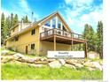 Charming chalet-style home with a large deck, surrounded by lush greenery and a stone retaining wall at 1176 Raven Ridge Rd, Idaho Springs, CO 80452