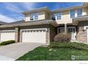 Exterior of townhome featuring a two-car garage and stone accents, set against lush greenery at 3000 E 112Th Ave # 102, Northglenn, CO 80233