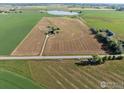 Aerial view of farmland showcasing a home, fields and a pond in the distance at 420 E County Road 10, Berthoud, CO 80513
