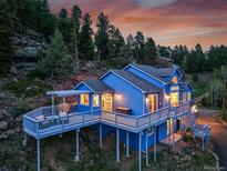 Stunning exterior shot of blue home featuring multiple decks and amazing sunset at 33633 Elk Run, Evergreen, CO 80439