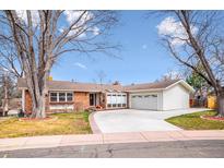 Charming single-story home with brick facade, attached garage, and a beautifully landscaped front yard and mature trees at 6854 S Prescott St, Littleton, CO 80120