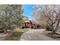 Inviting brick home with a circular driveway and mature trees against a blue sky at 1036 Lexington Ave, Westminster, CO 80023