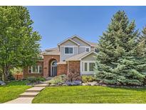 Charming two-story home featuring a brick facade, arched entryway, lush landscaping, and mature trees at 13901 Quail Ridge Dr, Broomfield, CO 80020