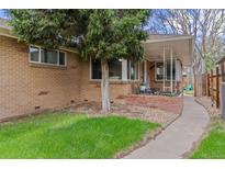 Charming brick home with a lush green lawn, mature tree, and covered porch area with seating at 3667 Hudson St, Denver, CO 80207