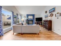 Bright living room features a brick fireplace, wood floors, and large windows with backyard view at 1236 Sequerra St, Broomfield, CO 80020