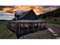Charming two-story home with a wrap-around porch, set against a stunning sunset sky, offers picturesque outdoor living at 8191 S Homesteader Dr, Morrison, CO 80465