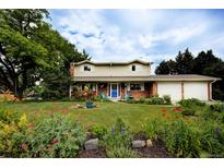 Charming two-story home with a well-manicured lawn, beautiful flowerbeds and a bright blue front door at 10373 W 75Th Ave, Arvada, CO 80005