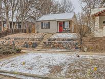 Charming home featuring a red front door, stone retaining wall and landscaped front yard with some snow at 3440 N Steele St, Denver, CO 80205