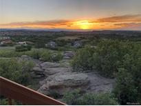 Scenic view of sunset over a distant town from a property's outdoor living space with native landscaping at 1995 Wingfeather Ln, Castle Rock, CO 80108