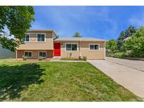 Inviting home featuring a bright red front door, a well-maintained lawn, and mature trees at 980 S Nile Way, Aurora, CO 80012