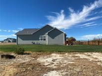 The backyard features a well-maintained lawn and a classic wooden fence under a sunny, partly cloudy sky at 51 W 6Th Pl, Byers, CO 80103
