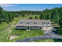 Expansive home with a large wraparound porch, manicured lawn, and an attached two-car garage at 3619 Estates Cir, Larkspur, CO 80118