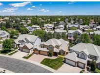 Stunning aerial view of a tan home with a beige tile roof surrounded by lush greenery and neighboring houses under a blue sky at 5416 S Hannibal Ct, Centennial, CO 80015