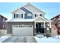 Charming two-story home with stone accents, a covered porch, and a two-car garage on a snow-covered lot at 1048 Larkspur Dr, Erie, CO 80516