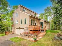 Charming home with a well-manicured lawn, stone accents, wooden deck, and an attached garage nestled amongst lush green trees at 2654 Sinton Rd, Evergreen, CO 80439