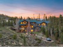 Stunning exterior shot of mountain home with a stone chimney, walkway and hot tub nestled amongst mature trees at 23 Verde Ct, Breckenridge, CO 80424