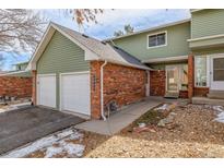 A home featuring a two-car garage, and a brick facade, with snow on the yard at 1922 Lydia Dr # 82, Lafayette, CO 80026