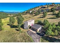 Stunning aerial view of modern home with mountain views, set on a grassy hillside with a detached two-car garage at 23924 Matterhorn Dr, Indian Hills, CO 80454