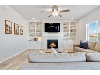 Bright living room with built-in shelving, a cozy fireplace, and modern ceiling fan at 12759 Buffington Trl, Parker, CO 80134