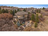 Stunning tan home with mature trees, stone accents, multiple patios, and mountain views at 1159 Buffalo Ridge Rd, Castle Pines, CO 80108