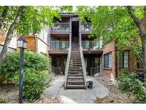 Inviting condo complex featuring brick and wood exterior, lush greenery, and a central staircase leading to upper units at 830 S Vance St # F, Lakewood, CO 80226