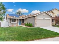 Charming home with a well-manicured lawn, stone accents, solar panels, and inviting blue door at 13244 Quivas St, Denver, CO 80234