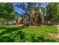 Brick apartment building nestled in lush green landscape with mature trees providing ample shade on a bright sunny day at 6455 E Bates Ave # 4-105, Denver, CO 80222