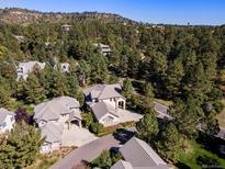 An aerial view of a luxury home nestled among trees in a lush, green, hilly neighborhood with blue skies at 3104 Ramshorn Dr, Castle Rock, CO 80108