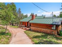 Charming exterior of a wooden home with brick accents, a green roof, and a well-maintained yard at 30122 Nancys Ln, Conifer, CO 80433