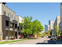 Street view of modern townhomes with trees in the foreground, and city buildings in the background, on a sunny day at 1323 Elati St # 3, Denver, CO 80204