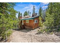 Charming wood cabin nestled amongst the trees with solar panels on roof and gravel parking in front at 542 Harris Dr, Idaho Springs, CO 80452