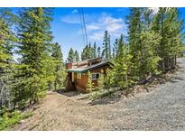 Quaint mountain cabin nestled amongst mature pine trees with solar panels on the roof at 542 Harris Dr, Idaho Springs, CO 80452