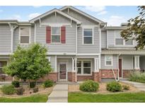 Charming gray townhome featuring a well-manicured lawn, garden beds and front entrance with brick accents at 5813 Ceylon St, Denver, CO 80249