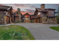Stunning mountain home featuring a stone and wood exterior, porte-cochere, and circular driveway at sunset at 220 Cottonwood Cir, Breckenridge, CO 80424