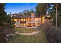 Elegant home featuring a stone chimney, large windows and a manicured lawn, nestled among mature trees at 67 Indigo Way, Castle Rock, CO 80108