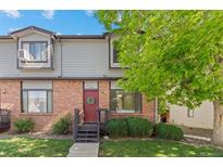 Charming townhouse with brick facade, red door, green wreath, and lovely front yard landscaping at 10693 W 63Rd Dr # 106, Arvada, CO 80004