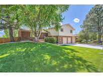 Landscaped front yard featuring a lush green lawn, mature trees, and charming two-story brick accents at 11410 W 72Nd Pl, Arvada, CO 80005