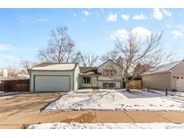 Light blue house with attached garage, snow-covered front yard, and mature trees at 6280 Zinnia St, Arvada, CO 80004