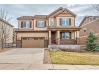 Two-story home with a tan exterior, brown shutters and trim, a front porch, stone accents, and a two-car garage at 3522 Harvard Pl, Broomfield, CO 80023