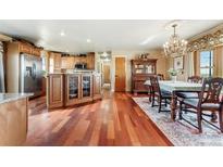 Open kitchen with an island with wood cabinets and hardwood floors into the dining room with chandelier lighting at 4295 S County Road 193, Byers, CO 80103