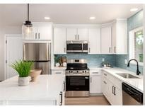 Bright kitchen with stainless steel appliances, white cabinets, quartz countertops, and a modern blue tile backsplash at 1011 Yeager Dr, Longmont, CO 80501
