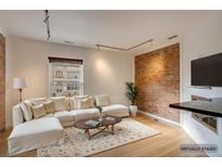 Cozy living room featuring a large sectional sofa, wood floors, exposed brick, and ample natural light at 2306 Glenarm Pl # 206, Denver, CO 80205