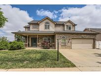 Charming two-story home featuring a covered front porch, brick accents, an attached garage, and a well-manicured lawn at 5483 Gunnison Dr, Frederick, CO 80504