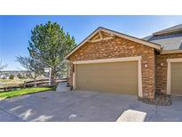 Attached two-car garage with stone facade and concrete driveway, next to a tree and a view at 7511 S Sicily Way, Aurora, CO 80016