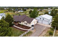 Charming ranch-style home featuring a large detached garage, manicured lawn, and white picket fence at 5685 Columbine Ridge Rd, Elizabeth, CO 80107