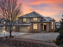 Charming two-story brick home with a three-car garage, landscaped yard, and inviting front entrance at sunset at 15652 W 79Th Pl, Arvada, CO 80007