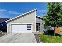 Charming home featuring a modern garage door, gray siding, green lawn, and a beautifully landscaped yard at 719 S Hoover Ave, Fort Lupton, CO 80621