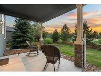 Covered patio features stone pillars, rocking chairs and views of the landscaped yard and sunset at 19067 W 57Th Dr, Golden, CO 80403