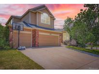 Inviting two-story home featuring a three-car garage, brick accents, and well-maintained landscaping under a beautiful sunset sky at 10089 Wynwood Way, Highlands Ranch, CO 80126